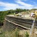 Construcción de un muro de suelo reforzado con geosintéticos, con personal y maquinaria trabajando sobre la coronación de la estructura