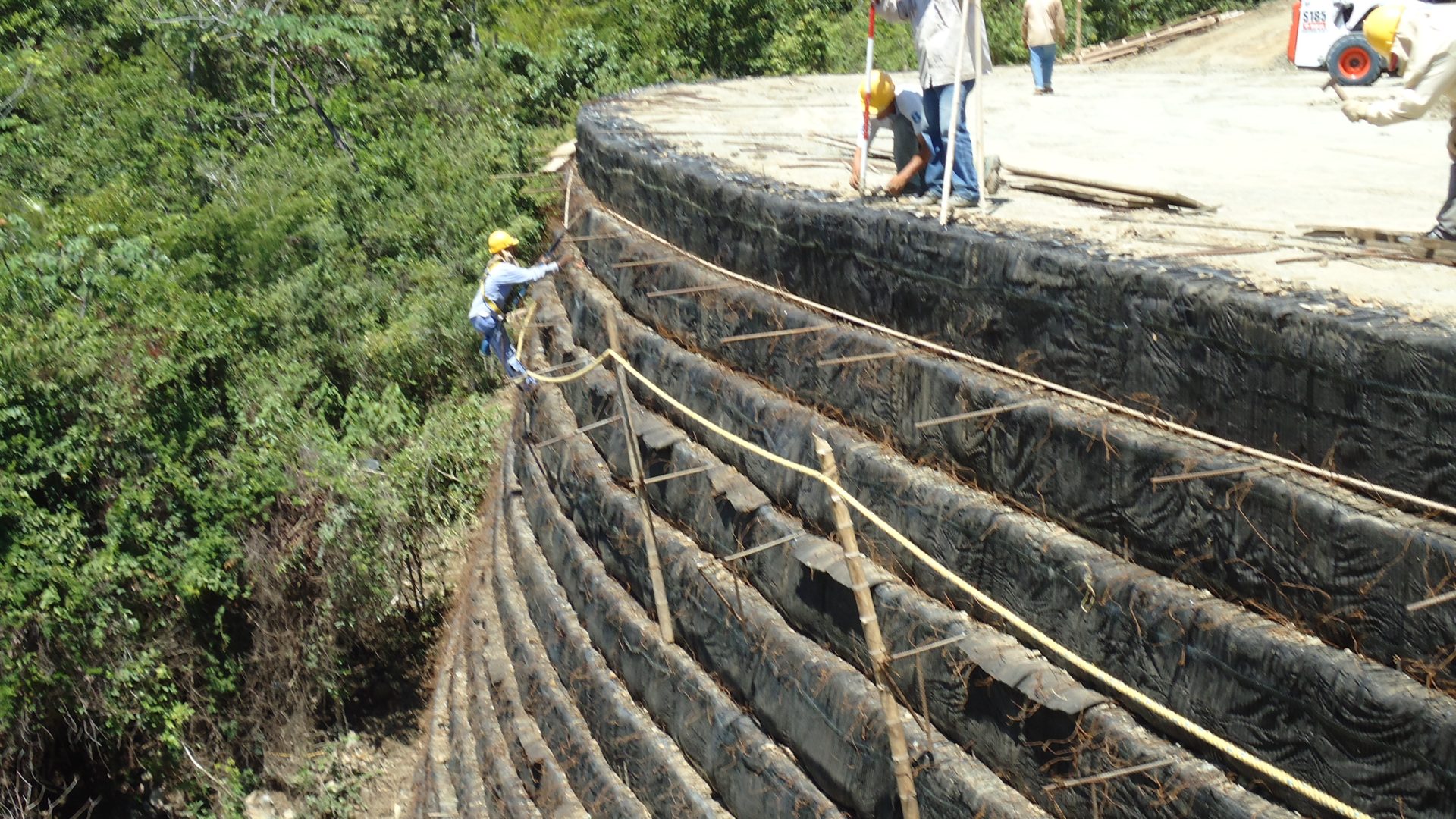 Muro armado en suelo reforzado (MSE) con geotextil tejido, con personal trabajando sobre el talud.
