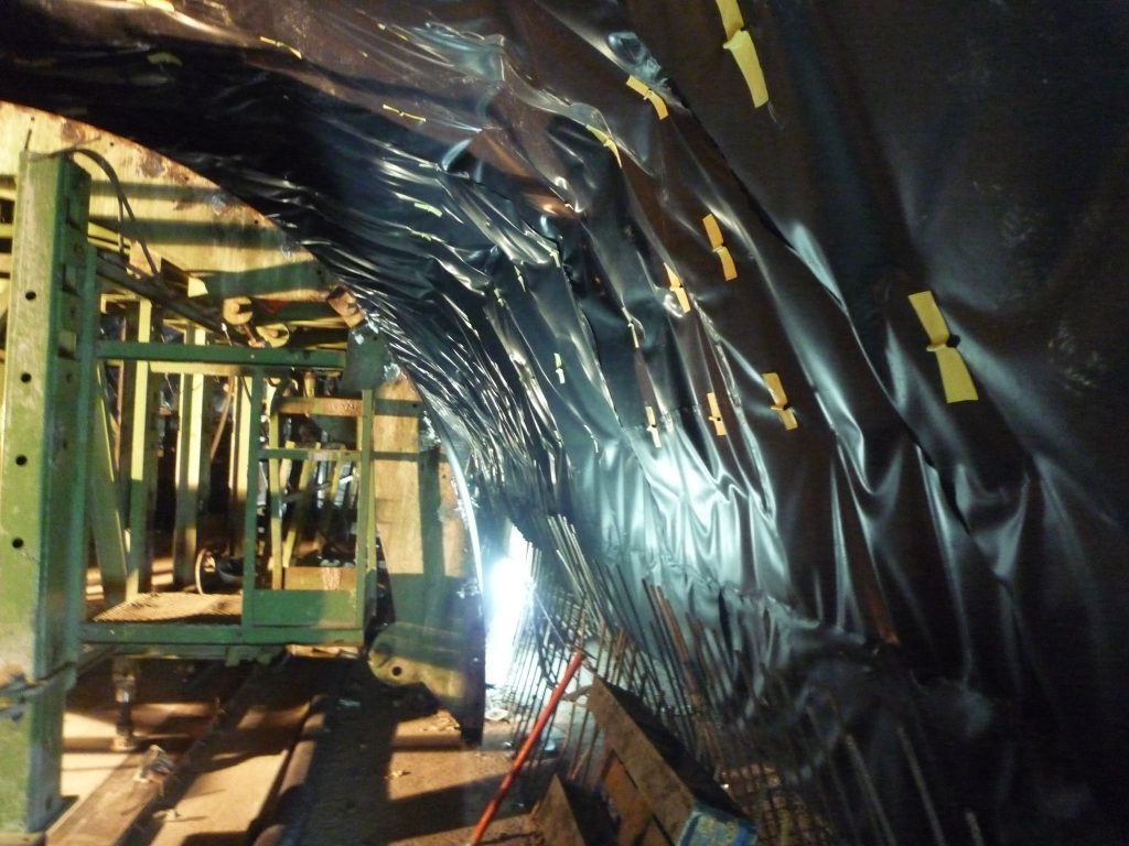 Vista interior de la bóveda de un túnel cubierta con una geomembrana negra, fijada con anclajes amarillos.