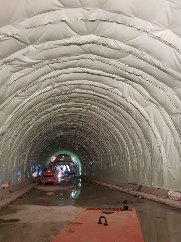 Interior de túnel en construcción con membrana impermeable clara y maquinaria al fondo